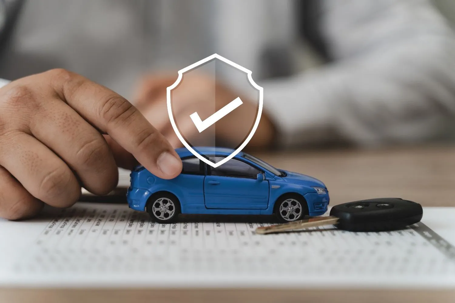 A hand resting on a blue model car beside a car key and a policy form