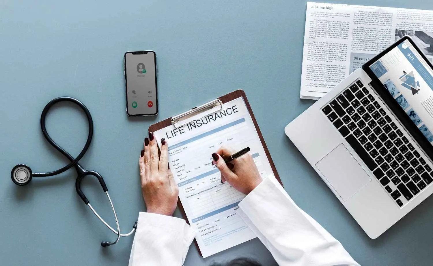 A life insurance form being filled in on a clipboard beside a laptop